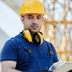 Homme en bleu de travail et casque jaune tenant un dossier — photo d’illustration